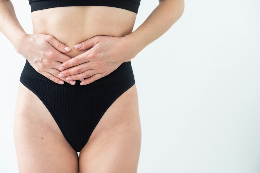 A woman in underwear holds her hands to her lower abdomen. Close-up. Beige background. The concept